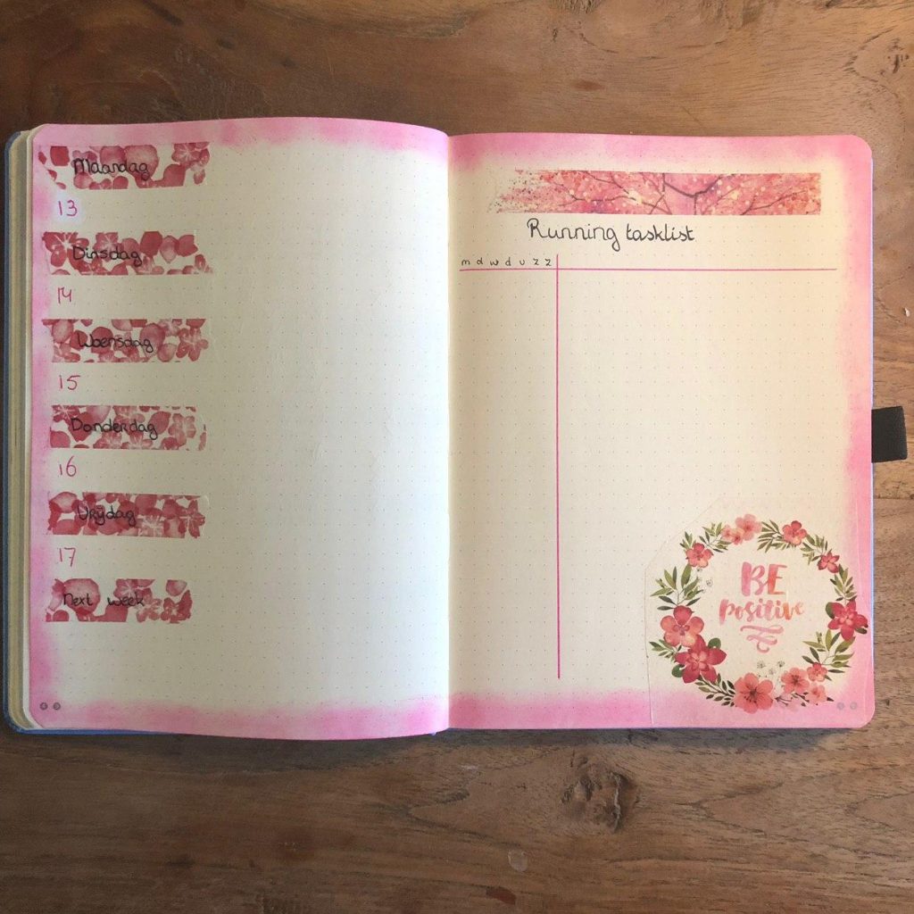 Open notitieboek met roze aquarelrand en bloemenstickers op houten oppervlak