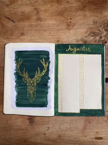 Open notitieboek met groene pagina en gouden hertontwerp op houten oppervlak