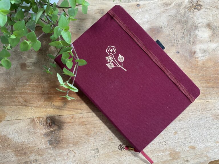 Een bordeauxrood notitieboek met wit bloemmotief op houten tafel
