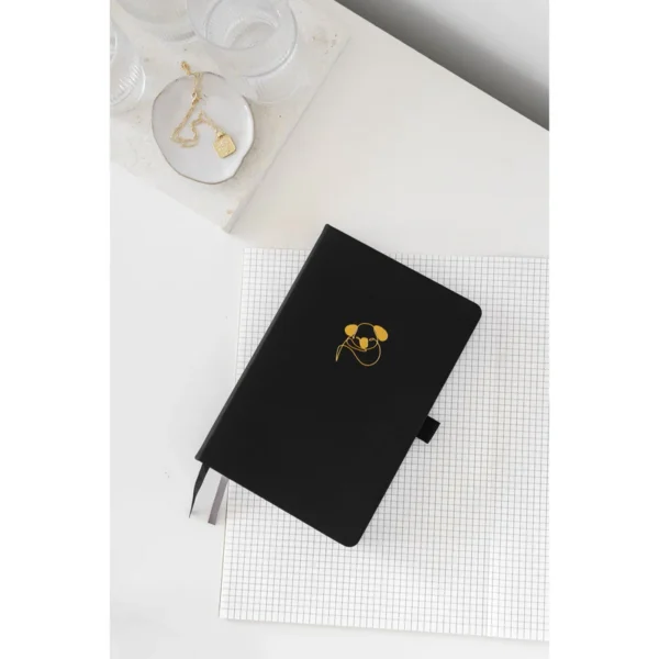 Zwart notitieboek met gouden koala-afbeelding op wit geruit papier