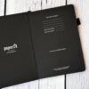 Zwart notitieboek van Paper24 open op wit houten oppervlak