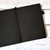 Zwart notitieboek met witte stippenpatroon opengeklapt op houten oppervlak