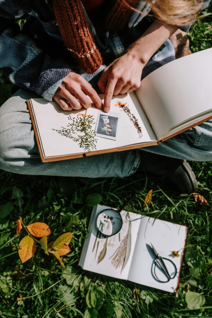 Persoon zittend op het gras met twee open notitieboeken en herfstbladeren