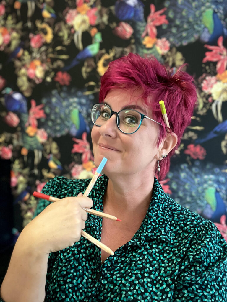 Vrouw met roze haar houdt drie potloden vast tegen een bloemenachtergrond