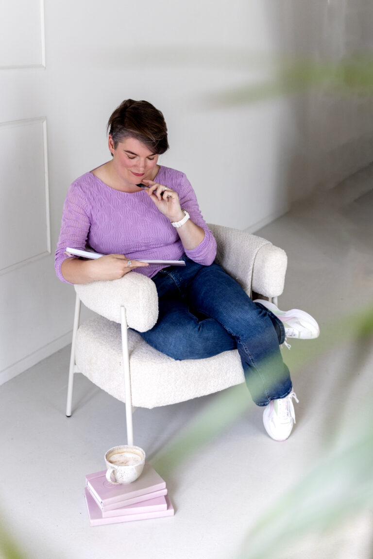 Vrouw zit in fauteuil en schrijft in notitieboekje met koffiekopje naast haar