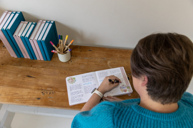 Persoon schrijft in een notitieboek op een houten tafel
