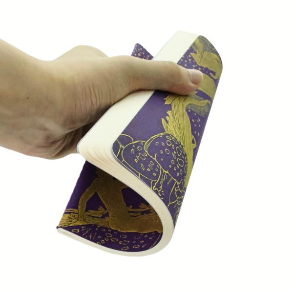 Hand houdt een paars notitieboek vast met gouden illustraties en dot grid papier