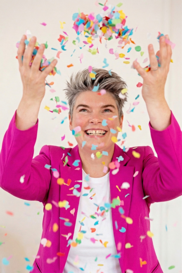 Vrouw in paarse jas gooit kleurig confetti omhoog tegen witte achtergrond